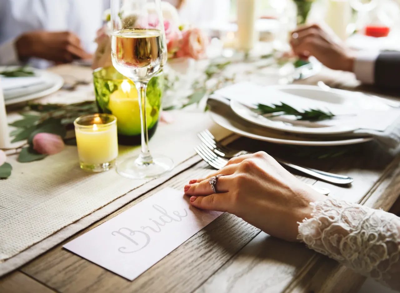 Bride's hand with engagement ring resting beside her place setting at a rehearsal dinner table