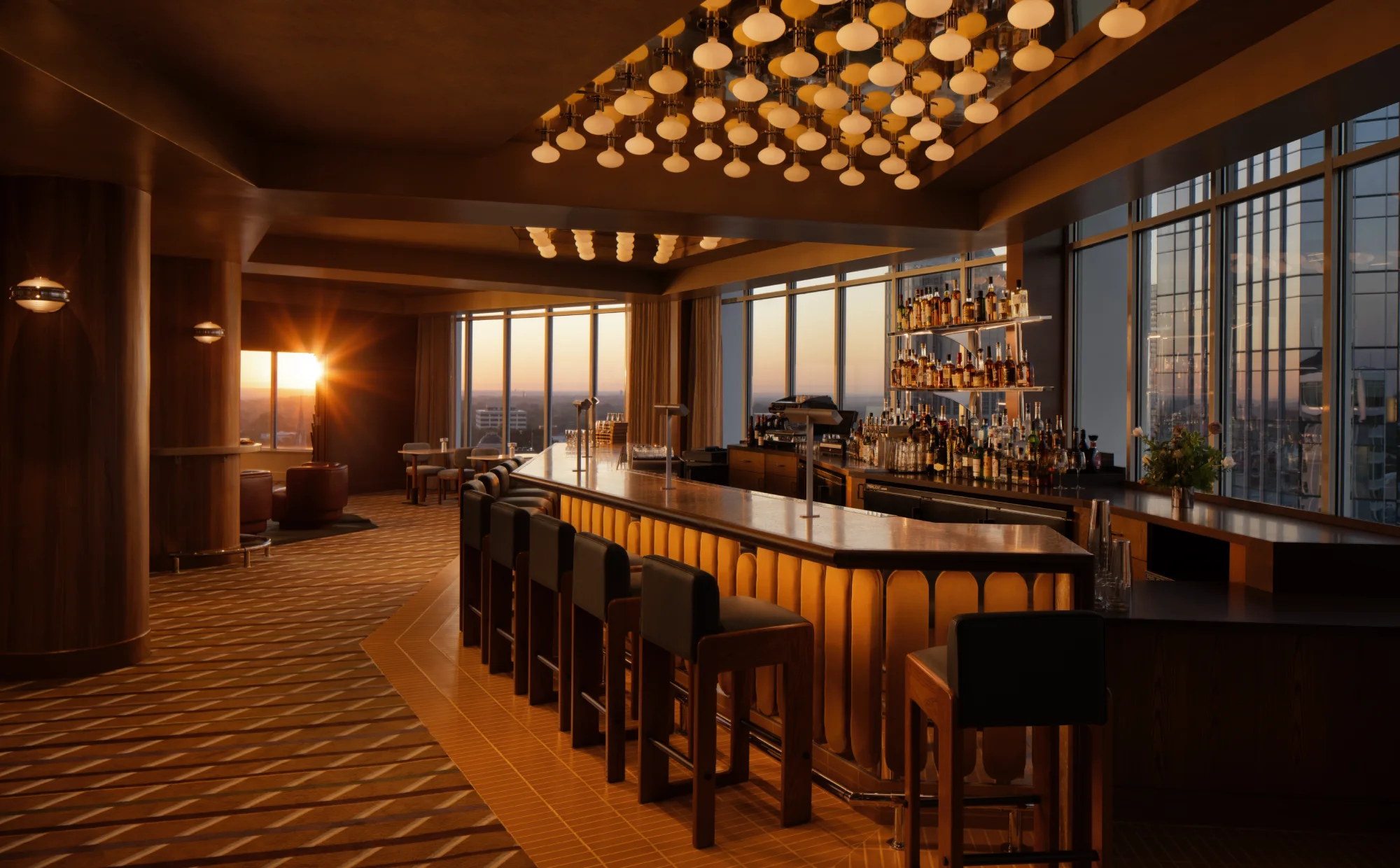 The High Ground Lounge bar glowing under golden pendant lights as the sun sets over Raleigh