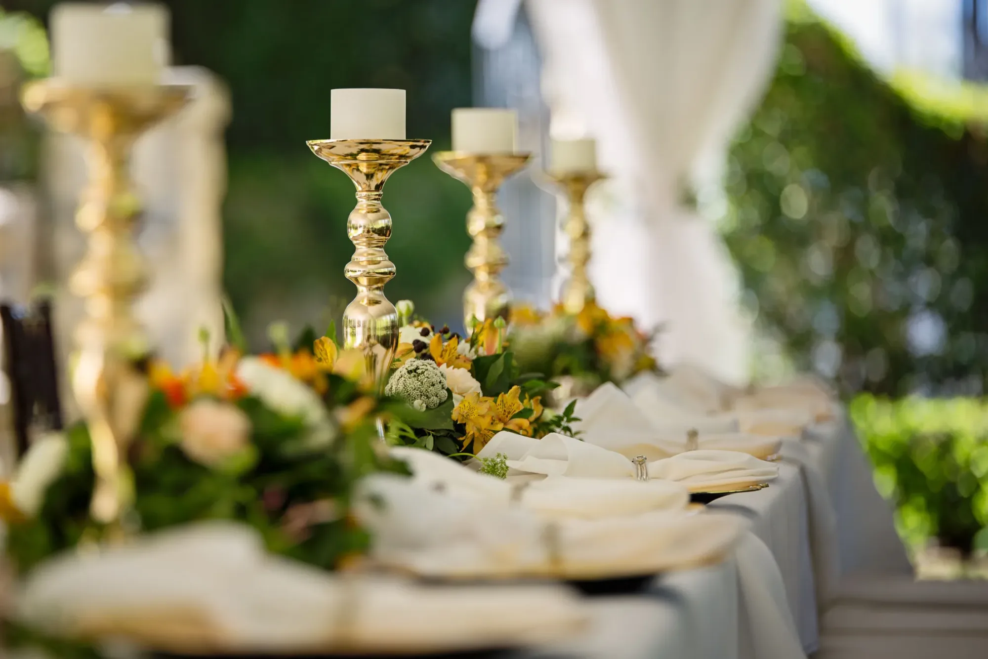 Garden table set with gold candlesticks and fresh floral runners for a wedding celebration